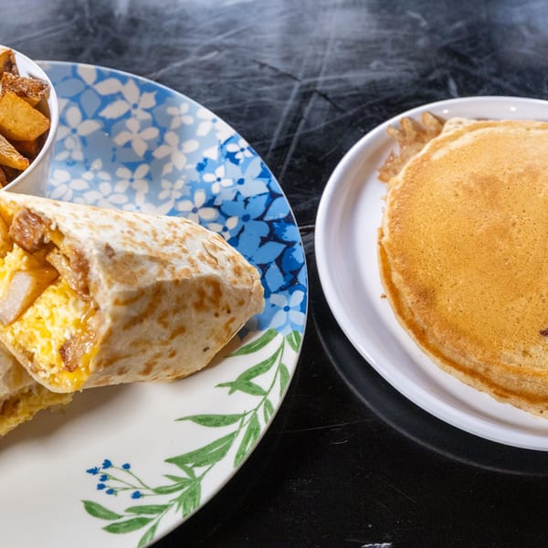 Breakfast burrito with home fries and a stack of pancakes on a dark table.