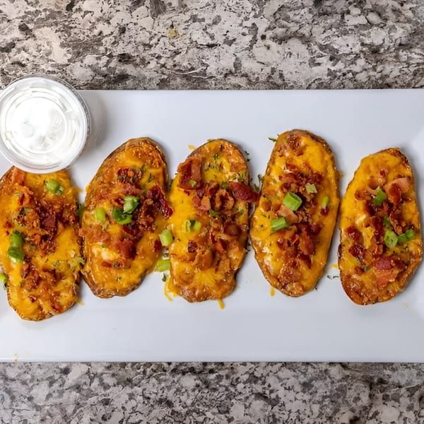 Five potato skins topped with melted cheese, bacon bits, and green onions, with a side of sour cream.