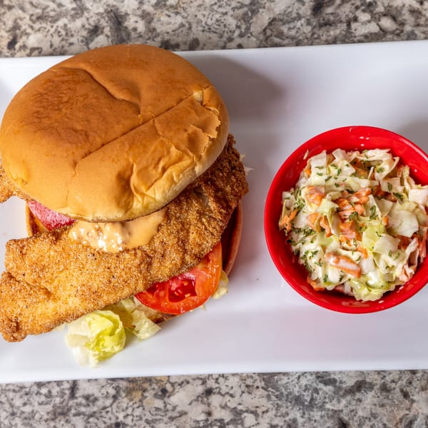 Crispy fried fish sandwich with lettuce, tomato, and sauce, served with a side of coleslaw.