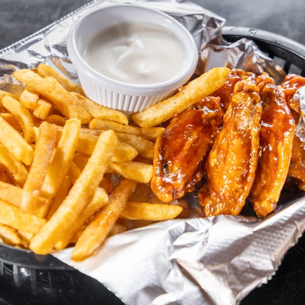 A basket of golden french fries, glossy barbecue chicken wings, and a side of dipping sauce.