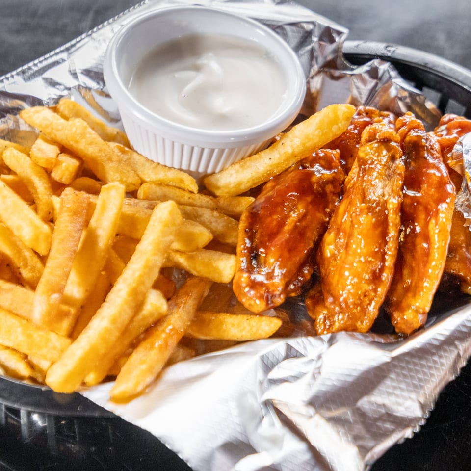 A basket of golden french fries, glossy barbecue chicken wings, and a side of dipping sauce.
